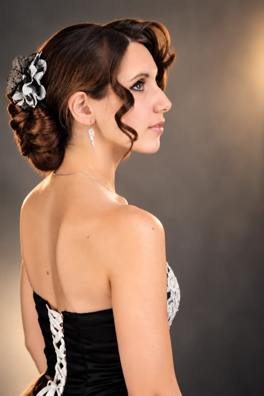 Profile portrait of a woman with brown hair styled in an updo, a black-and-white floral hair accessory, dangling earrings, and a strapless black-and-white outfit.